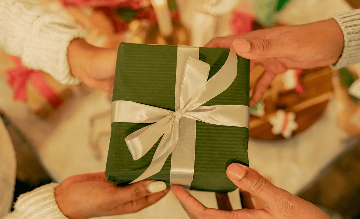 Two people exchanging a green gift wrapped with a white ribbon